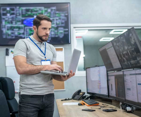 attention-focus-attentive-young-muscular-man-with-badge-laptop-standing-front-computer-monitors